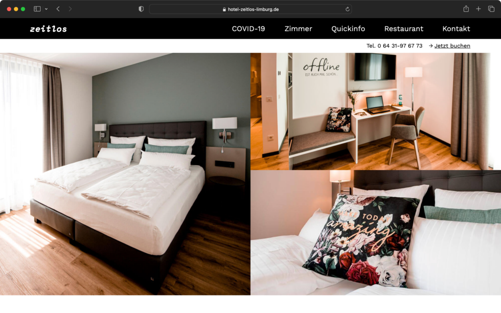 Hotelzimmer mit Doppelbett, Schreibtisch, Fernseher, Sitzbank und dekorativen Kissen in einem modernen, hellen Raum.