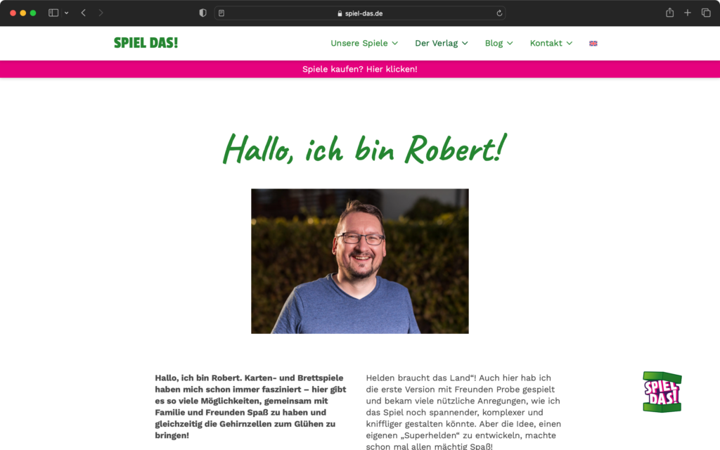 Porträtfoto eines lächelnden Mannes mit Brille und blauem T-Shirt vor unscharfem Hintergrund aus grünen Pflanzen.