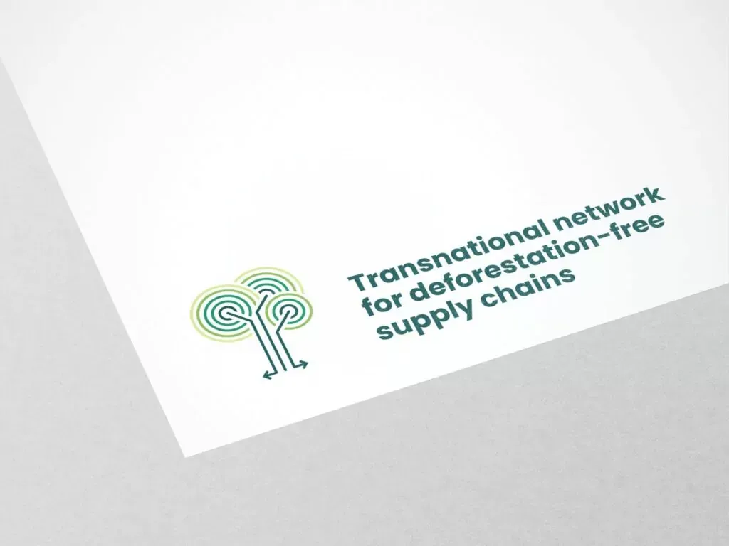 Logo mit stilisierten Bäumen und dem Text Transnational network for deforestation-free supply chains auf weißem Papier vor grauem Hintergrund.