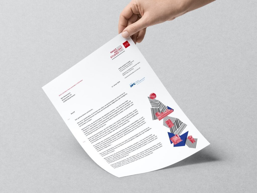 Hand hält ein Blatt Papier mit gedrucktem Text und farbigen grafischen Elementen auf grauem Hintergrund.