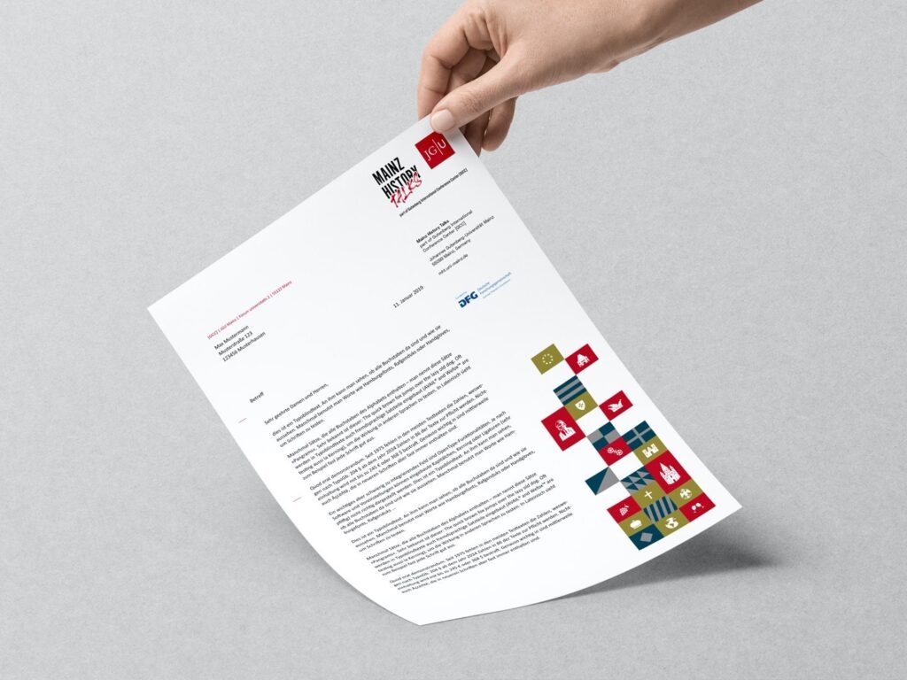 Hand hält ein Blatt Papier mit Text und buntem Logo auf grauem Hintergrund.