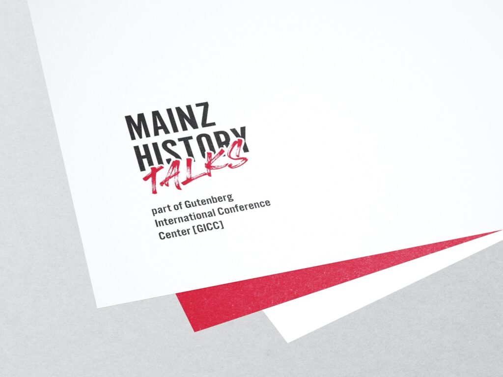 Logo mit dem Text Mainz History Talks part of Gutenberg International Conference Center GICC auf weißem und rotem Papier auf grauem Untergrund.