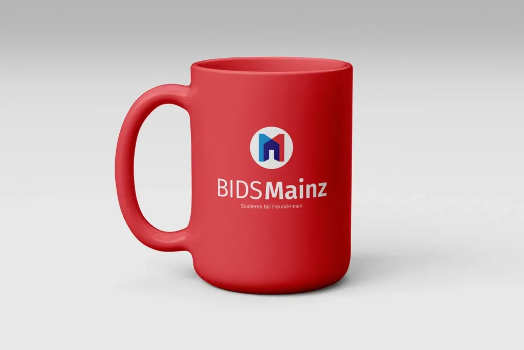 Rote Tasse mit dem Logo und Schriftzug BIDS Mainz und dem Text Studieren bei Freund*innen auf weißem Hintergrund.