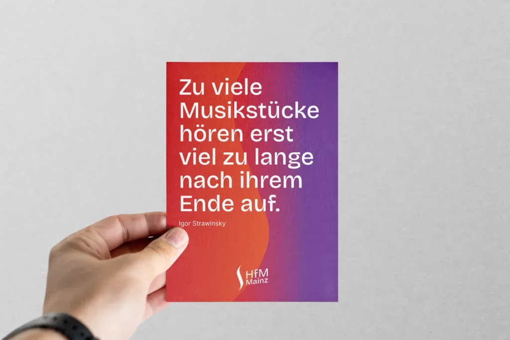 Hand hält eine Karte mit Farbverlauf von Rot zu Lila und weißem Text eines Zitats von Igor Strawinsky.