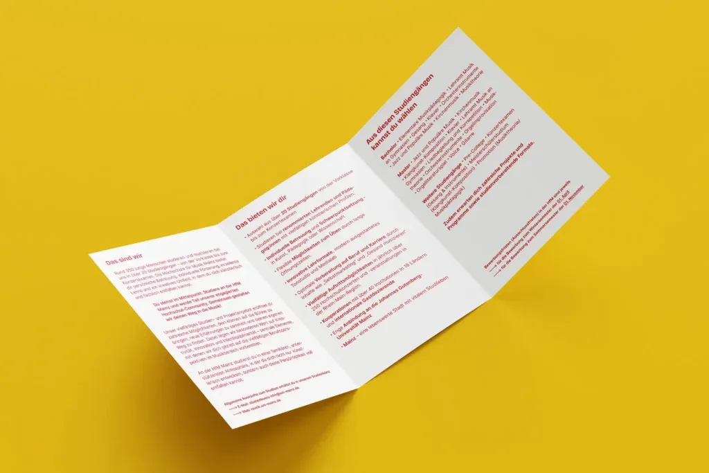 Auf einem gelben Hintergrund liegt ein aufgeklappter, weißer Flyer mit rotem Text, der Informationen zu Studienangeboten an der Hochschule für Musik Mainz enthält.