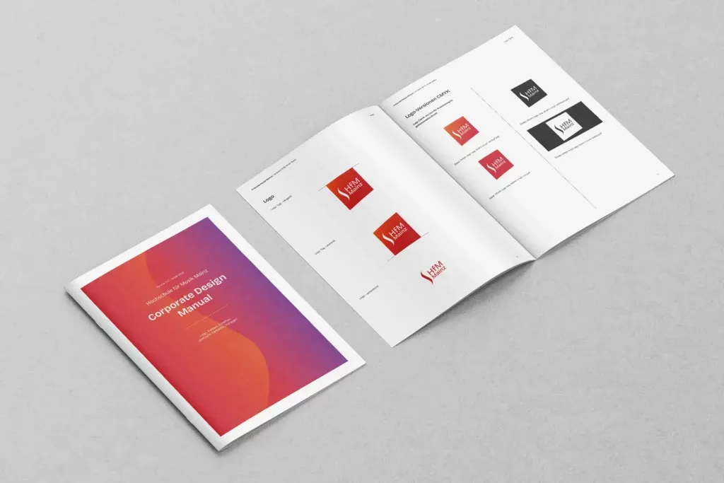 Zwei geöffnete Broschüren liegen auf grauem Untergrund, eine zeigt das Cover mit dem Titel Corporate Design Manual der Hochschule für Musik Mainz.